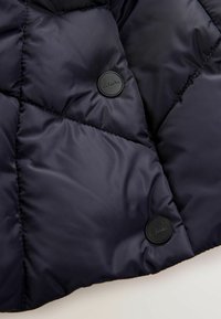 Giacca puffer blu navy in tessuto con motivo a diamante trapuntato. Presenta un bottone nero opaco con l'etichetta "Clarks" nella parte superiore sinistra. Texture liscia.