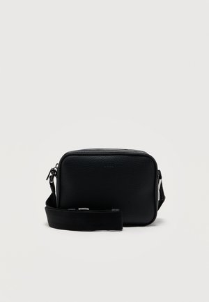Sac bandoulière rectangulaire en cuir noir avec sangle ajustable et fermeture éclair argentée sur un fond clair uni.