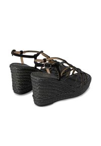 Sandalias de cuña negras con textura trenzada similar a la paja, que cuentan con tiras entrelazadas y una hebilla ajustable en el tobillo para un mejor ajuste.