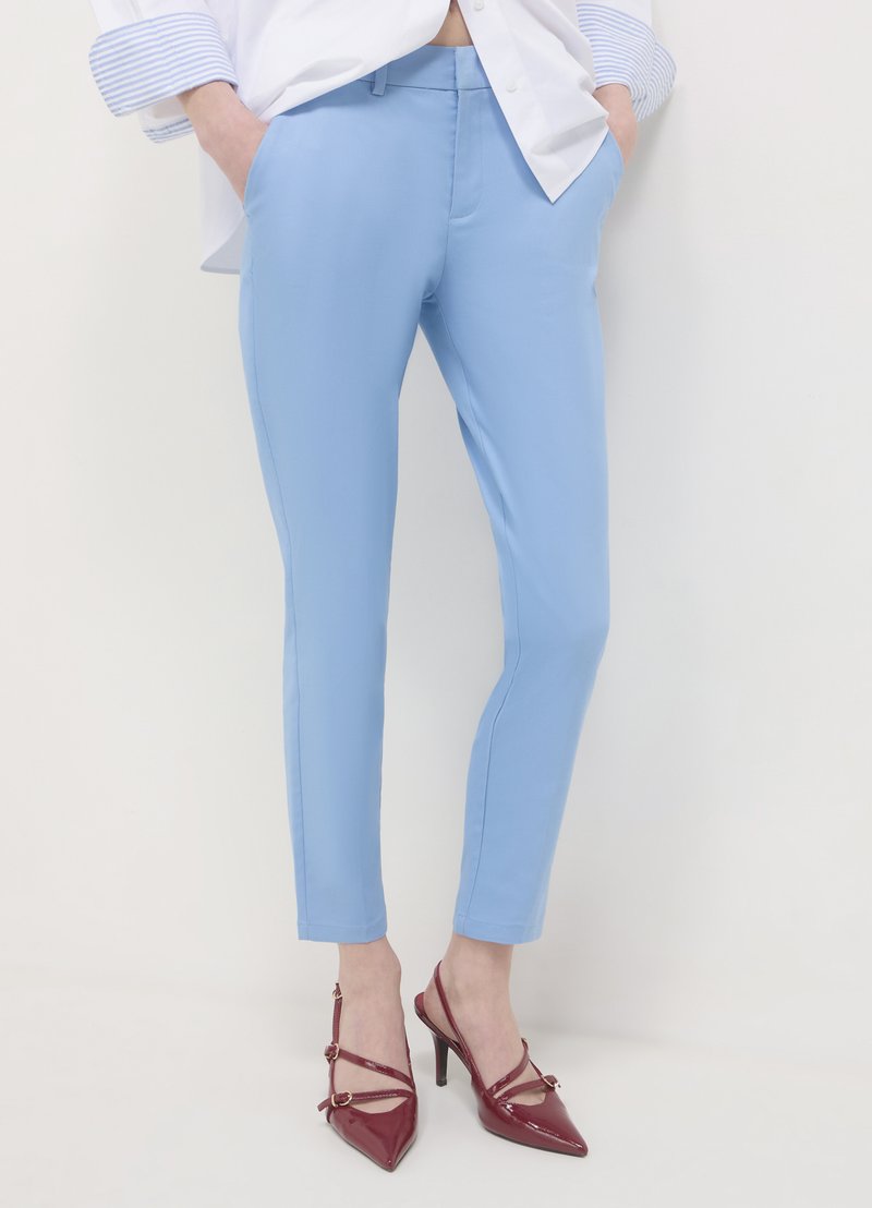 Hellblaue, maßgeschneiderte Hose mit engem Schnitt. Das Material wirkt glatt mit leichtem Glanz. Kombiniert mit burgunderroten High Heels.