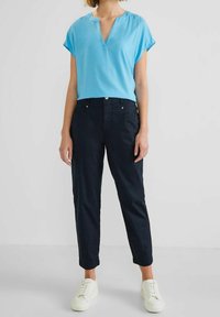 Haut bleu clair à manches courtes avec un col en V, associé à un pantalon navy foncé et des baskets blanches. Tissu doux avec une coupe décontractée.
