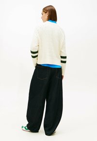 Pulover gros cu tricotaj în cablu, cu dungi verzi, purtat peste o cămașă albastră, asortat cu blugi negri largi și sandale verzi.