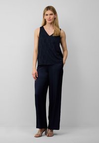 Haut sans manches bleu marine avec un motif en vagues texturé, associé à un pantalon large bleu marine. La tenue présente une coupe décontractée et des sandales à petit talon.