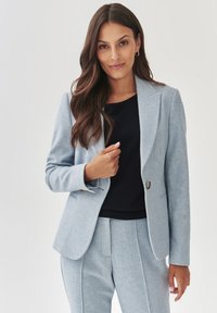 Světle modrý tailored blazer z texturovan�é tkaniny s výstřihem do špičky, uzávěrem na jedno knoflíček a dvěma předními kapsami, doplněný o tmavý top.