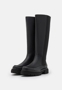 Botas de cuero negro hasta la rodilla con un acabado mate, suela de goma y paneles elásticos en los laterales para un ajuste ceñido. Diseño robusto con punta reforzada.