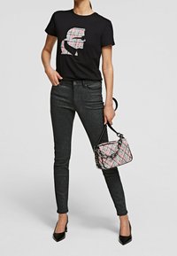Camiseta negra con un gráfico a rayas de colores, combinada con jeans oscuros y brillantes, y un pequeño bolso estampado con una cadena.
