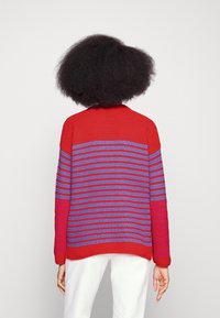 Maglione a righe rosse e viola con un motivo testurizzato, colletto rotondo e maniche lunghe. La gradazione di colore passa dal rosso al viola.