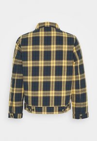 Žlutý a námořnicky modrý károvaný kabát s límcem, dlouhými rukávy a knoflíky na manžetách a lemu. Vyrobený z tkané látky s texturovaným povrchem.