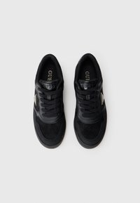 Baskets noires avec un mélange de textures mates et brillantes, présentant un design à lacets, un logo discret et une semelle rembourrée.