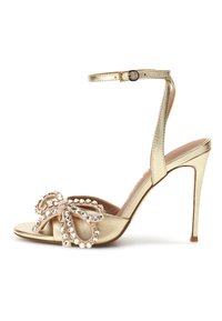 Goldfarbene High-Heel-Sandalen mit Knöchelriemen und offenem Zehenbereich, verziert mit einer dekorativen Schleife, die mit funkelnden Kristallen geschmückt ist.