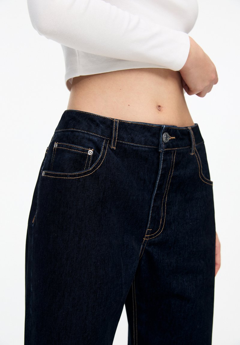 Dunkelblaue Denim-Jeans mit slim fit, ausgestattet mit orangefarbener Naht, vorderen und hinteren Taschen sowie einem Knopfverschluss an der Taille.