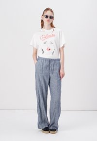 Hvid bomulds t-shirt med grafisk print af en kvindes ansigt, parret med lyse grå, løstsiddende bukser med elastisk talje og sorte sko.