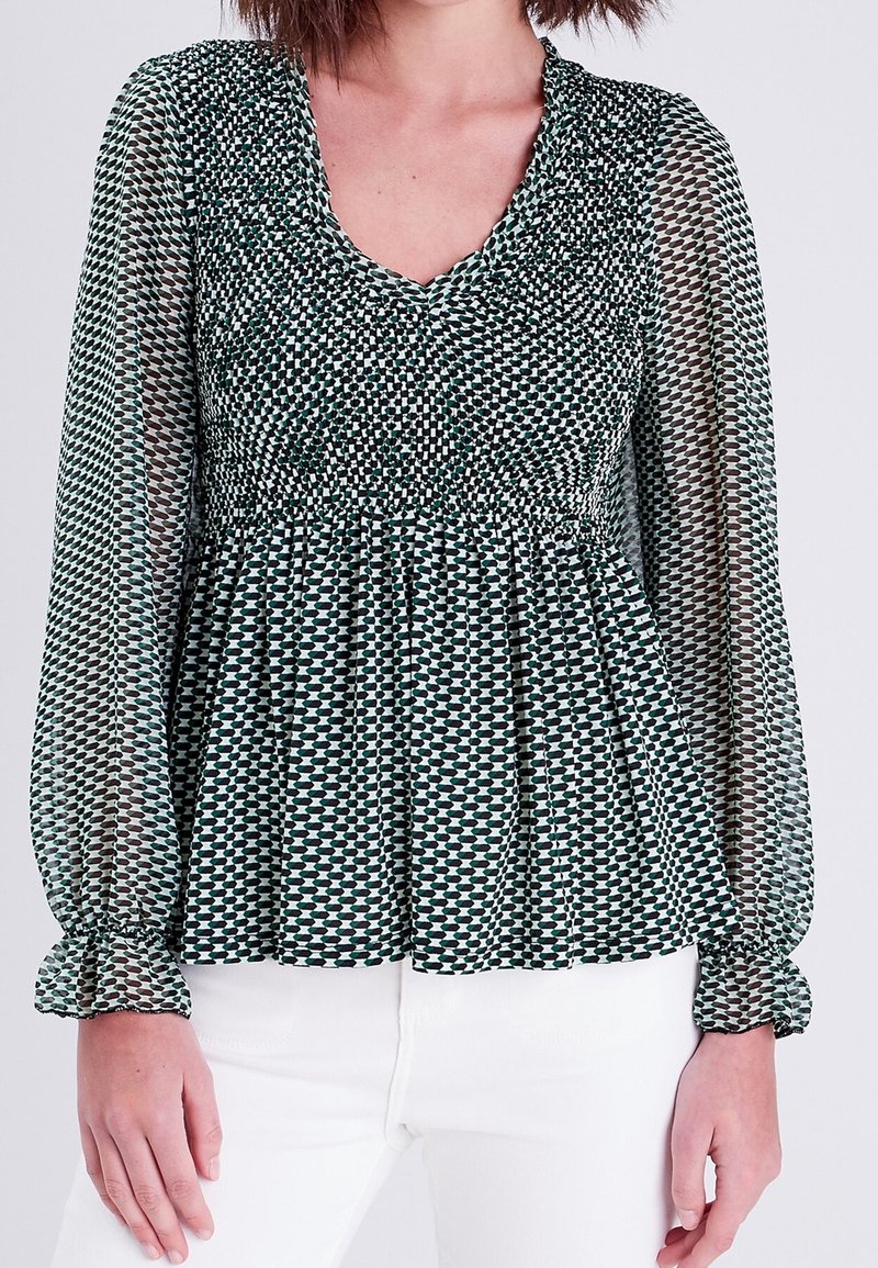 Blouse à motifs verts et crème avec manches longues et transparentes, taille froncée smockée et encolure en V. Tissu texturé avec une coupe fluide.