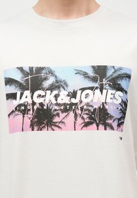 T-shirt blanc avec un graphisme rectangulaire de palmiers au coucher du soleil aux couleurs pastel et le texte "JACK & JONES" en surimpression.