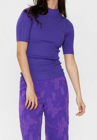 Lila ribbad topp med korta ärmar och hög hals, kombinerad med lila mönstrade byxor med blomdesign. Jämn och slät textur över hela plagget.