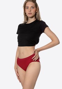 Sous-vêtements en coton rouge avec une texture lisse et un léger stretch. Design taille haute associé à un crop top noir ajusté.
