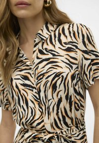 Chemise à manches courtes en tissu léger avec une base beige, présentant un motif rayé tigre noir et orange et une fermeture à boutons.