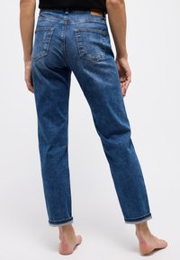 Modré džíny z denimu se střihem rovného nohavice. Obsahují dvě zadní kapsy a ohrnuté manžety. Materiál vypadá mírně texturovaně a opotřebovaně.