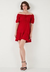 Red off-the-shoulder dress with puff sleeves, gathered bodice, and tiered hemline. Styled with black strappy heels. Smooth fabric texture.