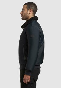 Herrebomberjakke i mørk marineblå med en myk svart krage, glidelåslomme på siden og ribbestrikkede mansjetter, med et merkevarelogo-merke.