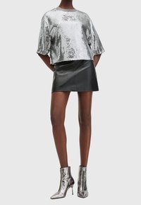 Top in paillettes argento con maniche corte, abbinato a una mini gonna in pelle nera. Modello indossa stivali metallici argento con punta a cono.