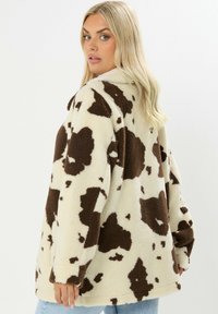 Crème- en bruine fleecejack met koeienprint, lange mouwen, relaxte pasvorm en textuurstof. De zoom eindigt op middel- heuphoogte.