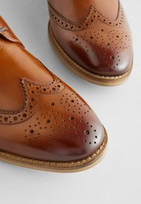 Chaussures en cuir marron avec détails en brogue. Dotées d'un bout lisse et de motifs texturés. Construction Goodyear welt avec une semelle durable.