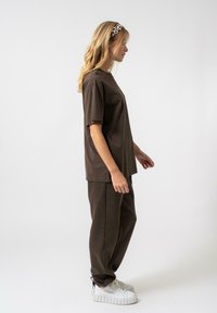 Barna pamut póló, laza fazonnal, amelyhez illő joggingnadrág és fehér sportcipő társul. A modellen leopárdmintás fejpánt található.