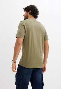T-shirt in cotone verde oliva con collo rotondo e maniche corte, caratterizzato da un design semplice e una texture liscia. Senza motivi o accenti visibili.
