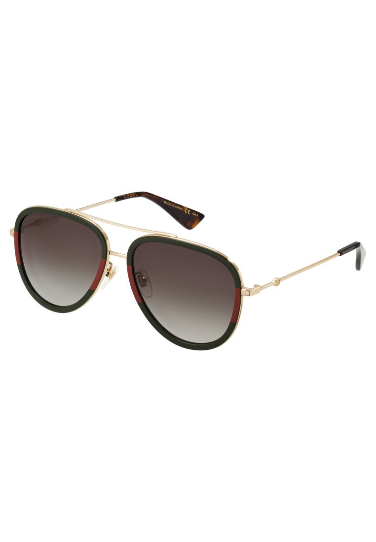 Aviator-stil solbriller med gullfarget metallramme, grønne og røde akenter, mørke gradientlinser og en definert geometrisk form.