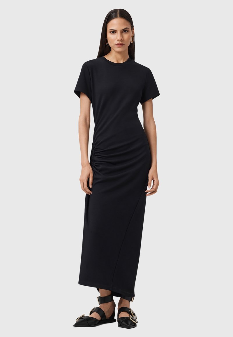 Maxi dress nera a maniche corte, con dettaglio arricciato sul lato, texture liscia e silhouette dritta. Accentuata da sandali.