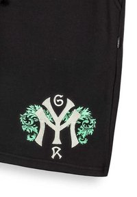 Zwarte shorts met ingewikkelde groene en zilveren borduring. Het ontwerp bevat gestileerde letters en decoratieve loofaccenten.