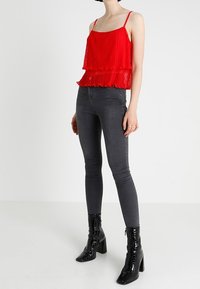 Haut rouge à couches avec texture plissée, bretelles ajustables, associé à un jean skinny foncé et des bottines en cuir verni noir à talons carrés.