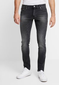 Svarta slim-fit jeans i denim med subtil blekning, slitna detaljer och en standard femfickorsdesign. Bärs med vita sneakers.