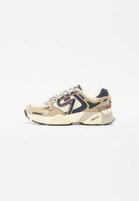 Beige en marineblauwe sport sneaker van mesh en suede materialen, met getextureerde overlays, een witte tussenzool, gedurfde rode accenten en patroonveters.