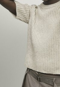 Beige geripptes Strickoberteil mit kurzen Ärmeln und weitem Rundhalsausschnitt. Die Textur ist weich und leicht dehnbar, was eine lockere Passform erzeugt.