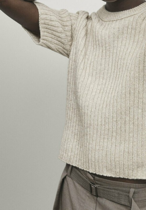 Beige geripptes Strickoberteil mit kurzen Ärmeln und weitem Rundhalsausschnitt. Die Textur ist weich und leicht dehnbar, was eine lockere Passform erzeugt.