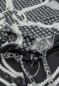 Tissu noir avec un motif blanc de chaînes, cordes et motifs circulaires. Le matériau semble lisse avec une finition légèrement brillante.