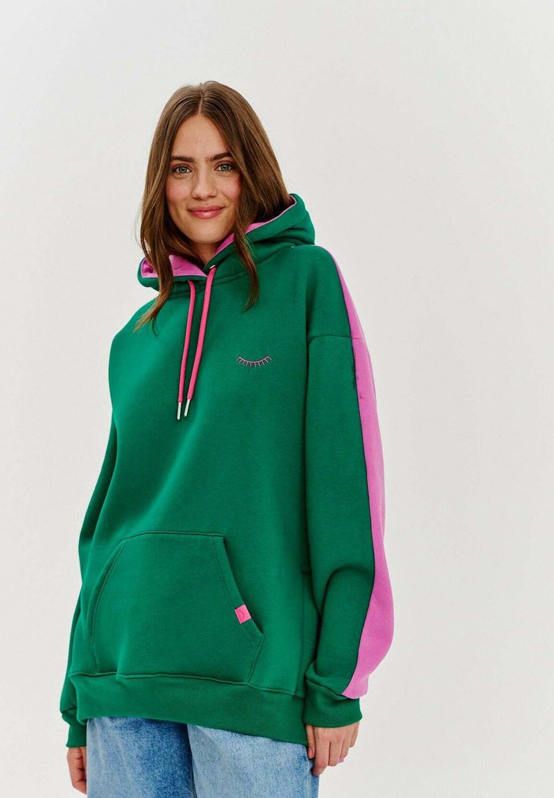 Zelená mikina s kapucňou a ružovými bočnými panelmi, má predné vrecko, ružové šnúrky a malý vyšitý detail v tvare rias.