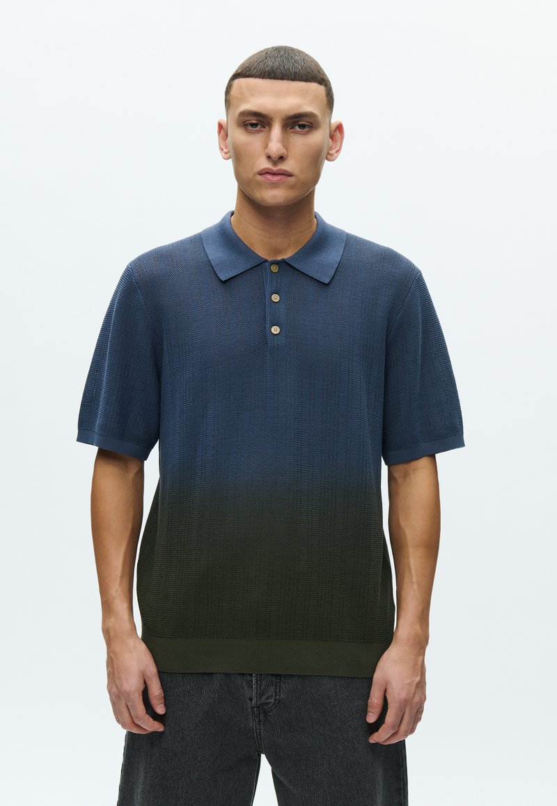 Πόλο με κοντό μανίκι και υφή πλεκτού σε μπλε χρώμα που εξασθενεί σε πράσινο. Διαθέτει γιακά και πατιλέτα με τρία κουμπιά.