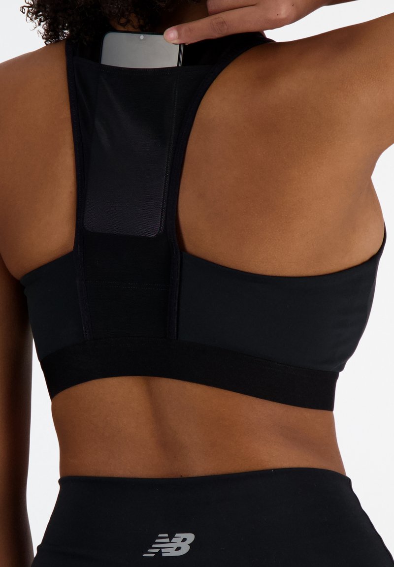 Soutien-gorge de sport noir avec un design dos nageur, fabriqué en tissu doux, avec une bande élastique et une poche pour téléphone à l'arrière.