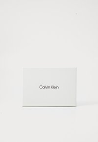 Scatola bianca con una finitura liscia, con il testo "Calvin Klein" in nero, centrato davanti. Design minimalista, forma rettangolare.