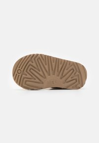 Suela de zapato de goma marrón claro con un patrón texturizado y estriado, y un logo circular. Presenta un dibujo prominente para un mejor agarre y estabilidad.
