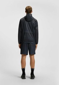 Navy waterproof jacket with hood, elastic hem; paired with dark shorts. Black socks with white lettering, and black footwear. Smooth texture.