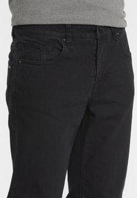 Black denim jeans with a slim fit, featuring a five-pocket design, subtle stitching accents, and a classic button closure at the waistband.