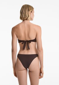 Rjav bikini komplet z bandeau zgornjim delom, ki ima vezanje zadaj, in nizkimi hlačkami. Gladka tekstura, minimalistična zasnova, brez vzorcev ali okraskov.