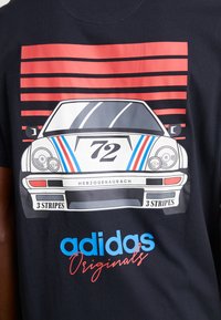 Melna T-kreka ar klasiskas automašīnas grafiku, kurā ir skaitlis 72. Virs tā sarkanas un zilas svītras, bet "adidas Originals" bieza balta un zila teksta formātā.