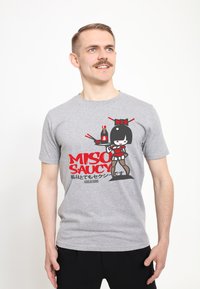 Camiseta de algodón gris con un gráfico de dibujos animados de un personaje sosteniendo salsa de soja, con el texto rojo "MISO SAUCY" y acentos en negro.