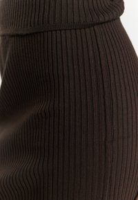 Braun geripptes Strickgewebe in einem figurbetonten Design mit vertikalen Linien und glatter Textur. Der Bund ist oben umgeschlagen.