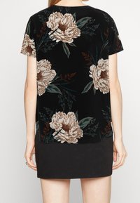 Černý květinový top s velkými béžovými pivoňkami a zeleným listím. Vyrobeno z měkké látky, volnějšího střihu a krátkými rukávy.